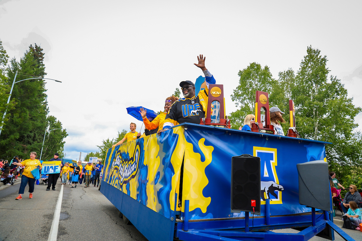 Darryl Lewis Sr. waves to the crowd as he stands next to the Nanook Rifle Team's NCAA championship trophies on board the UAF float for the 2023 Golden Days Parade in downtown Fairbanks.