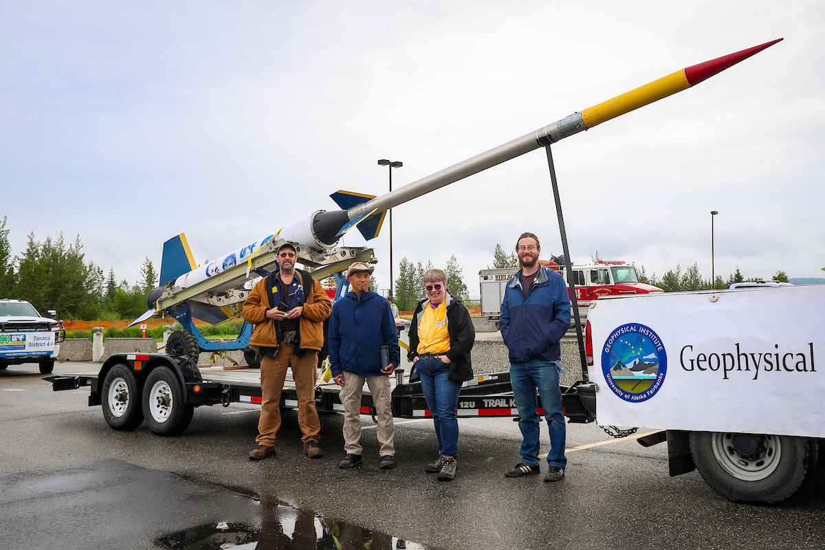 Members of the UAF Geophysical Institute stand beneath a test rocket from the Poker Flats Research Range before pulling it through downtown Fairbanks for the 2023 Golden Days Parade.