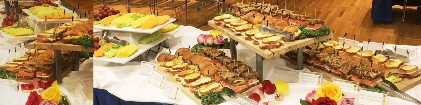Catered food spread of sliced fruits, sandwiches and flower arrangements