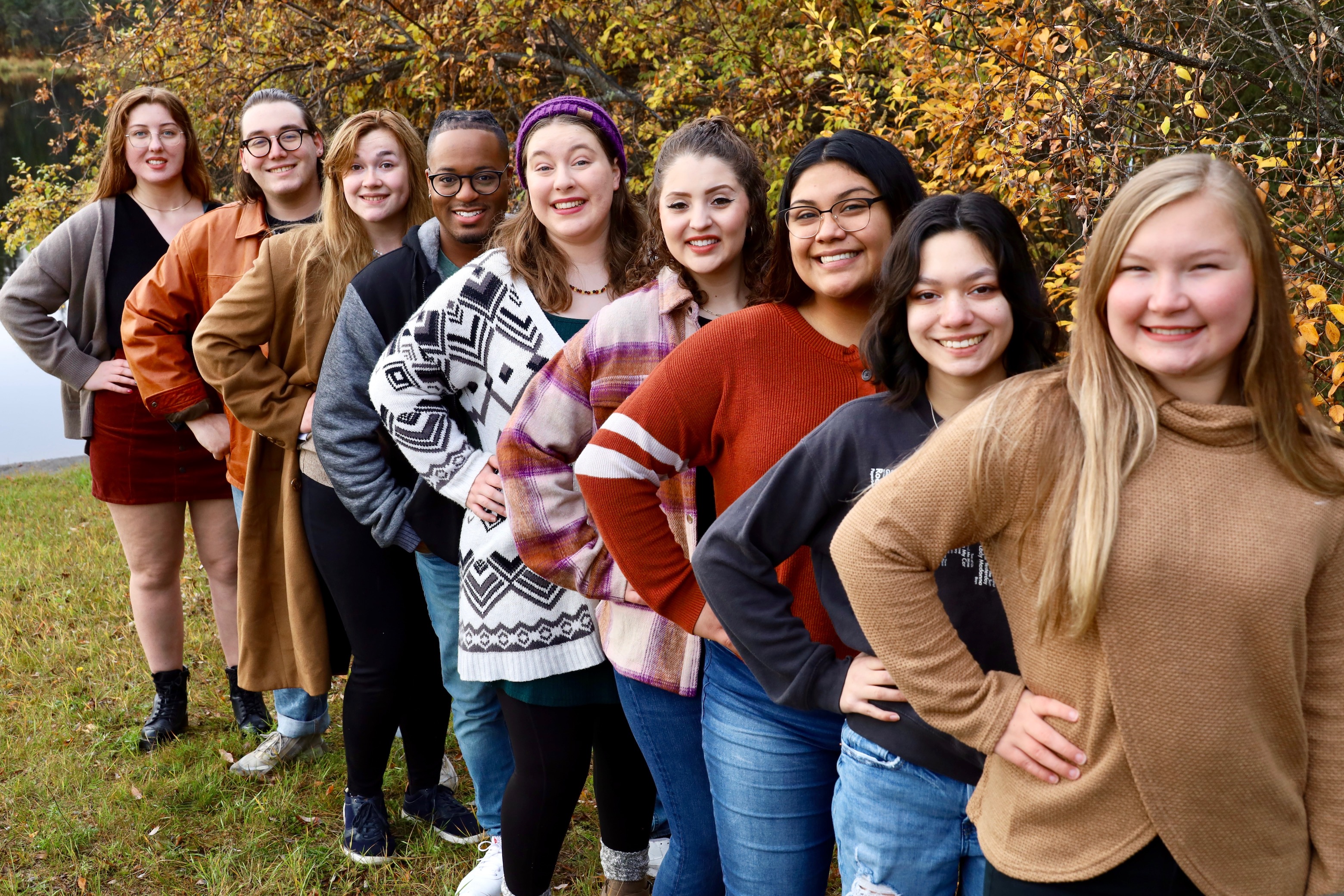 Music students stand in a line outside in front of the autumn foliage