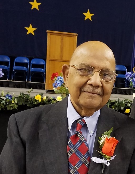 Headshot Banarsi Lal in front of a stage with the Alaska flag hanging in the background