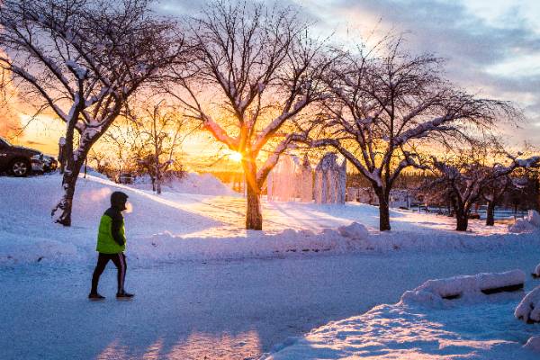 Student walks across the snow covered UAF Troth Yeddha' campus in Fairbanks as the sun is low on the horizon