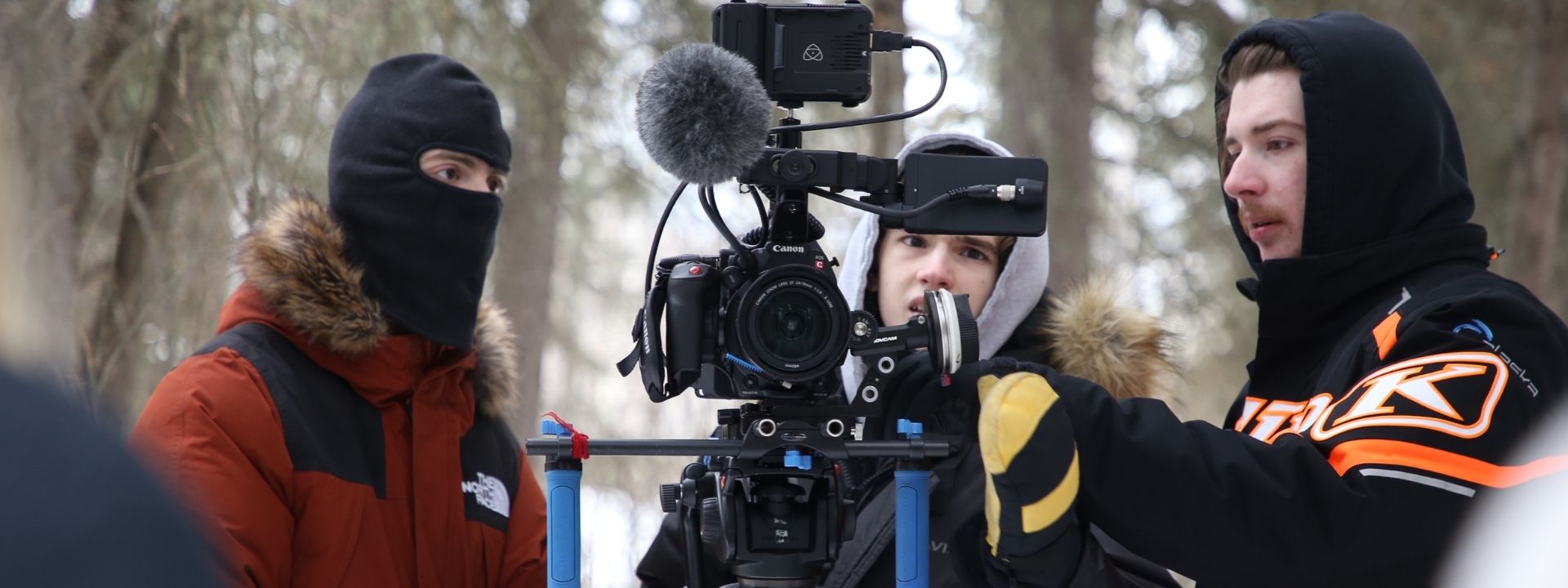 Behind the scenes on the set of MEND. Three film students gather around a camera. UAF Photo by Maya Salganek