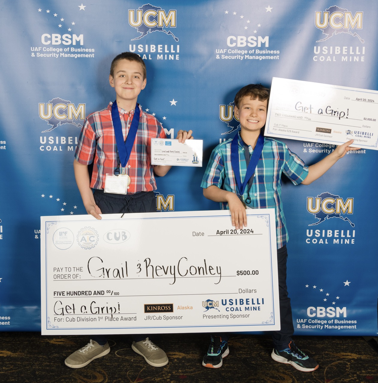 Two brothers, Grail and Revy Conley smile while holding up three checks.