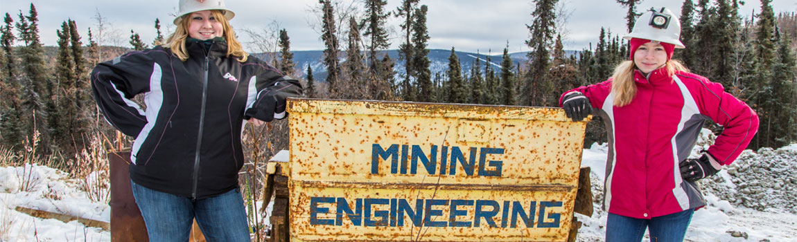 A pair of UAF mining engineering students pose ear a mining cart outside the Silver Fox Mine Lab