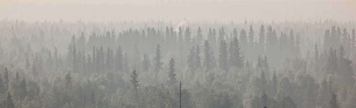 In the smoke filled distance, a stream of water spray is seen in the midst of an Alaska wildfire.
