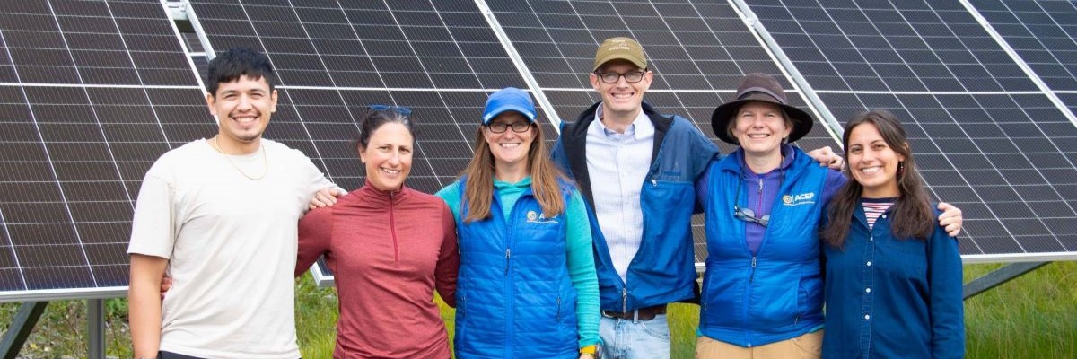 People stand smiling in front of solar panels