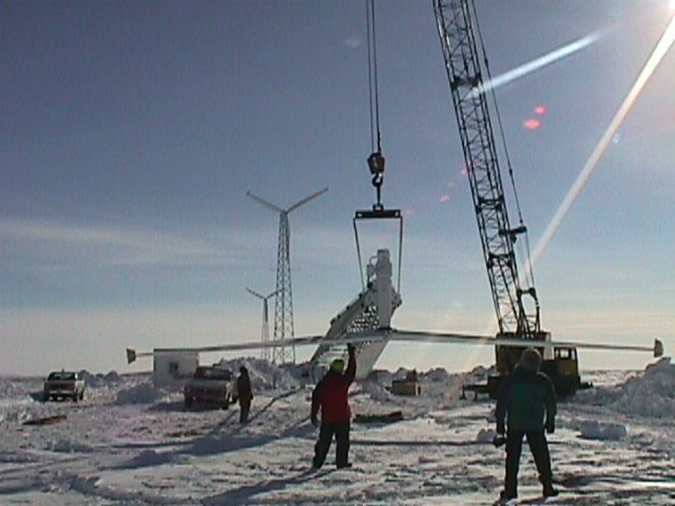 Crane lifts wind turbine on a cold clear late winter day in the Arctic.