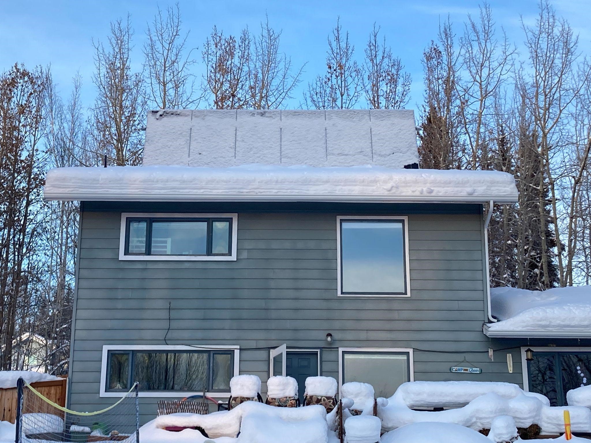 House with roof-top mounted angled solar panels covered in snow.