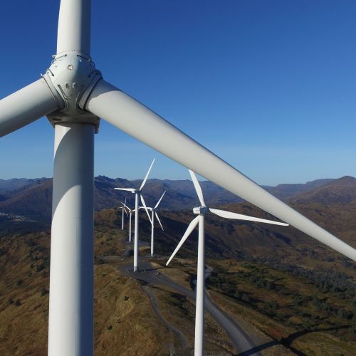 Drone photo taken of the center of a wind turbine on a clear summer day in the mountains. Several other wind turbines visible in the distance