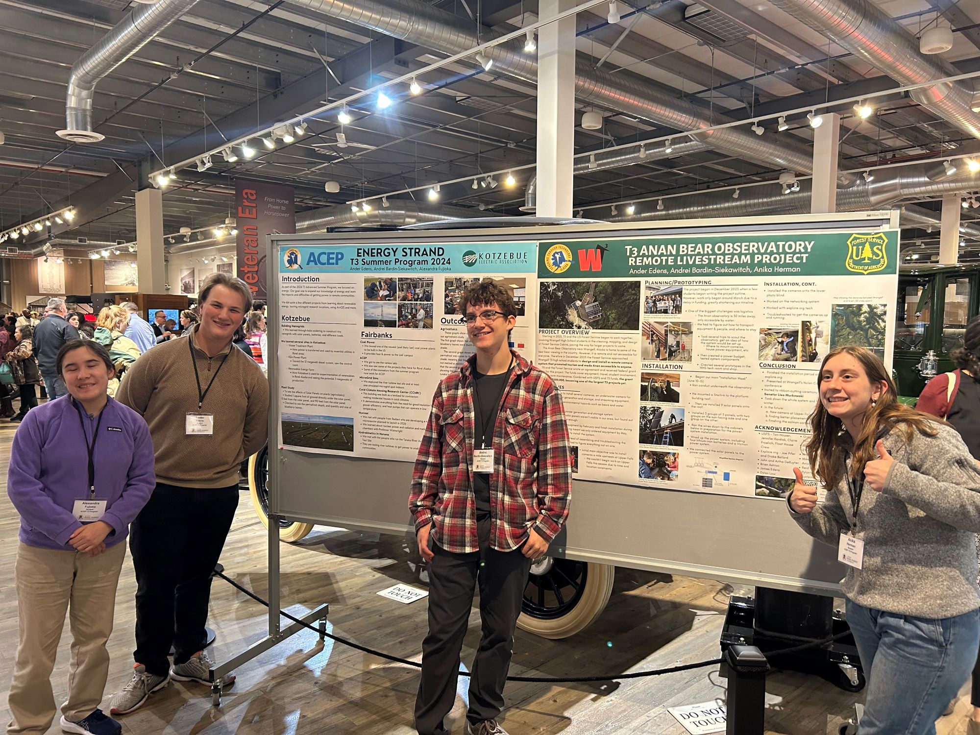 Students stand in front of scientific posters smiling and giving a thumbs up