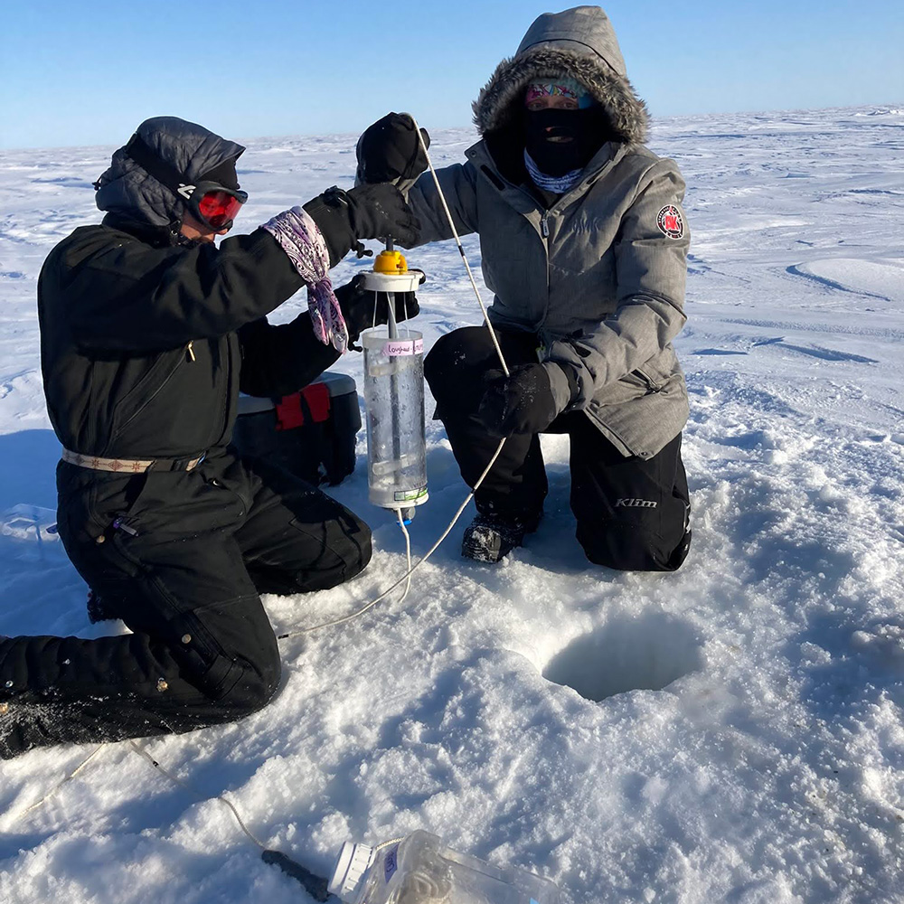Two researchers working with equipment on the ice.