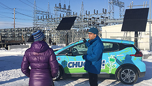 Two people dressed warmly standing by an EV and electrical grid.