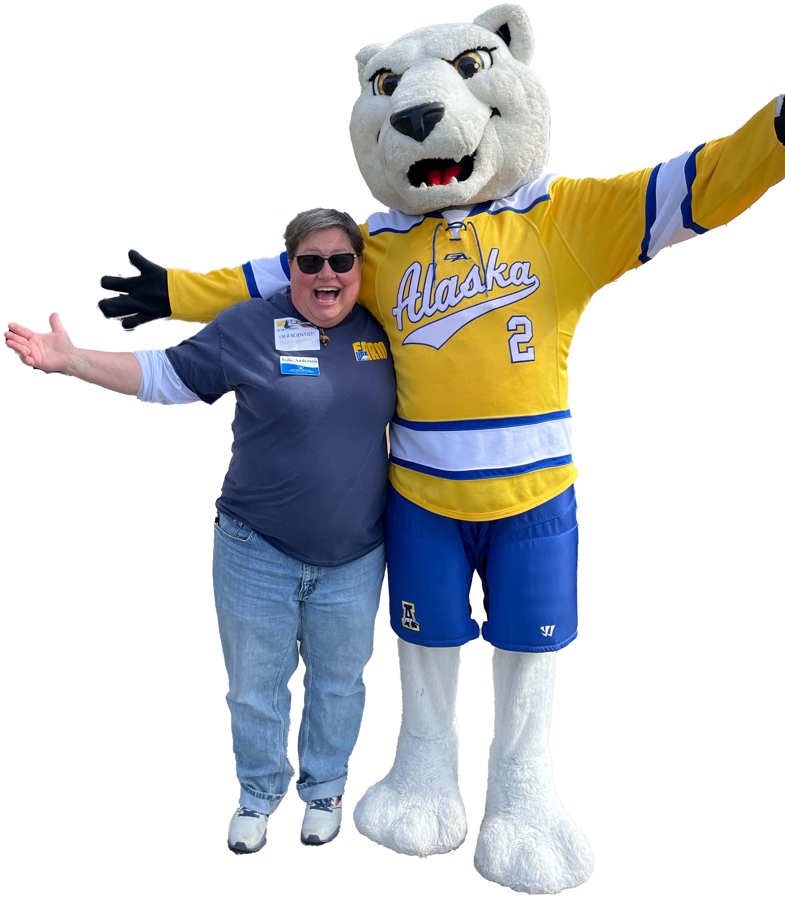 The director, Jodie Anderson, wearing a blue shirt UAF Farm shirt, jeans and sunglasses posing with Nook UAF's nanook mascot repping blue and gold. Both look real happy!