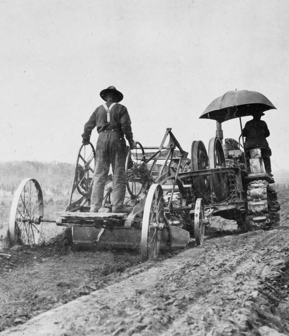 Black and white photo of a man riding an old-timey tractor