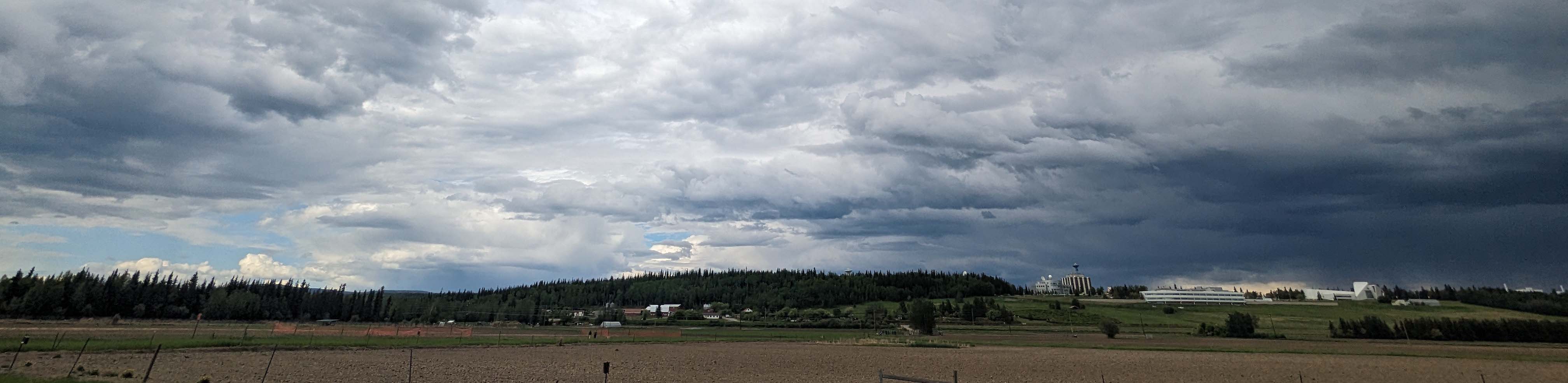 Dark blue stormclouds gathering above UAF campus in the background and the Experiment Farm fields in the foreground