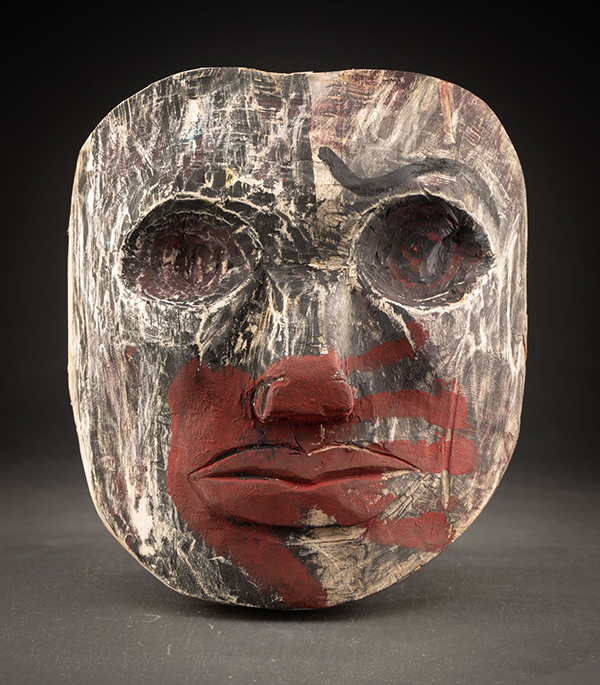 dark carved mask with a red handprint over the mouth