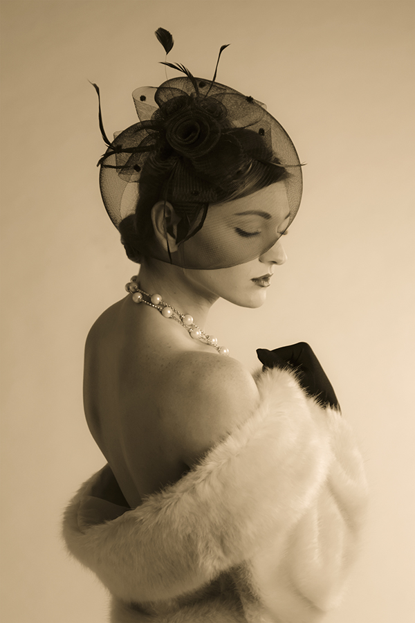 A sepia portrait of a woman with a pearl necklace in a fur stole and black netted cap