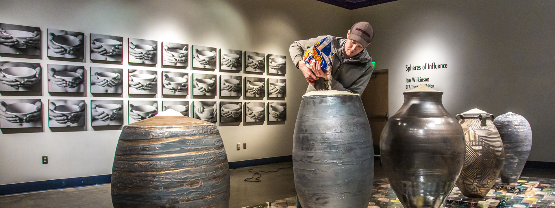 Art major Ian Wilkinson pours uncooked rice into the top of one of his ceramic pieces in the UAF Fine Arts gallery. His BFA thesis project, Spheres of Influence, raised more than $18,000 for the Fairbanks Food Bank through the sale of his 1,200 bowls. UAF Photo by Todd Paris