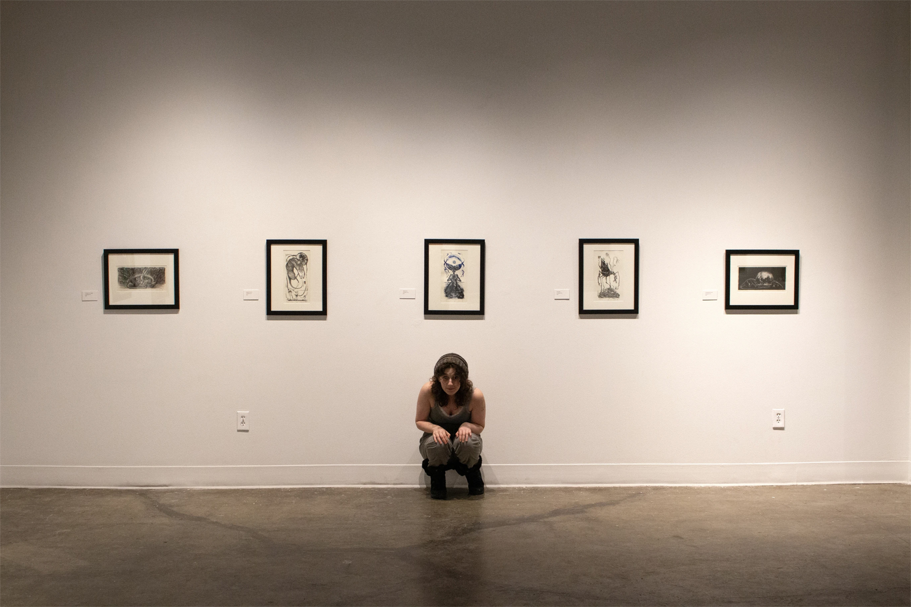 Chana Stern poses under a series of lithographs at the reception for "Pilgrimage of the Revenant", courtesy of the artist