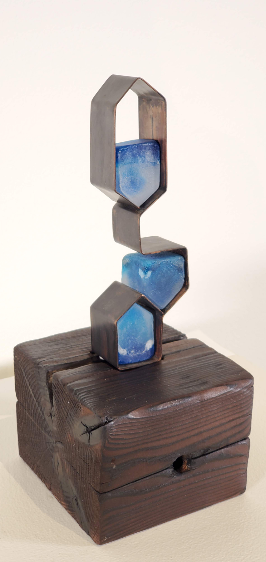 Three house-shaped blue cast glass structures nested in a copper sculpture. Image courtesy of the artist