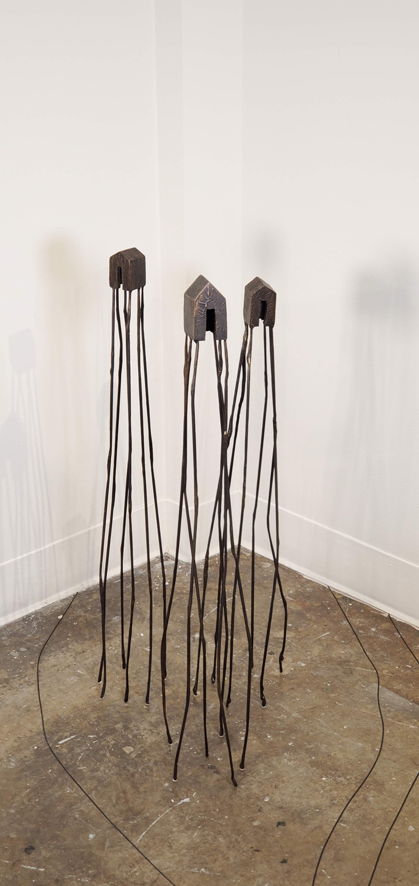 Three bronze houses atop long bronze stilts, image courtesy of the artist