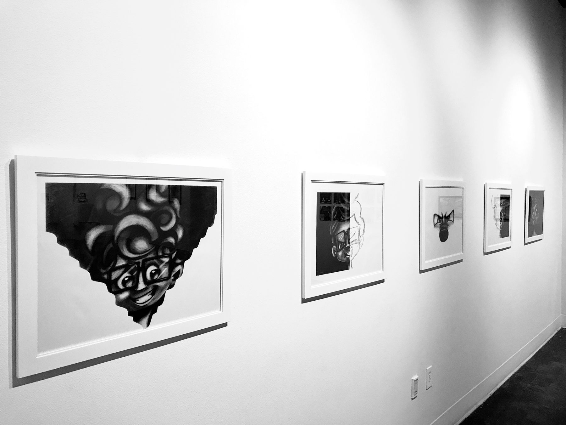 Looking down the gallery wall at a row of framed black and white character drawings from The Art of the Mudsuckle Ritual thesis exhibition, image courtersy of the artist