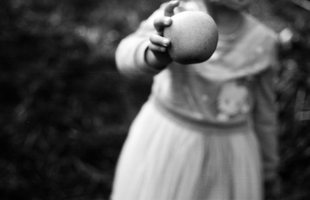 Black and white photo of a girl in a dress holding an apple, image courtesy of Kathryn Reichert