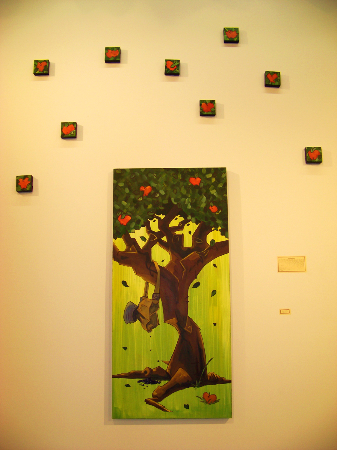 A large painting of an apple tree with smaller paintings of apples scattered over the gallery wall around it. Photo credit: Lucas Elliott