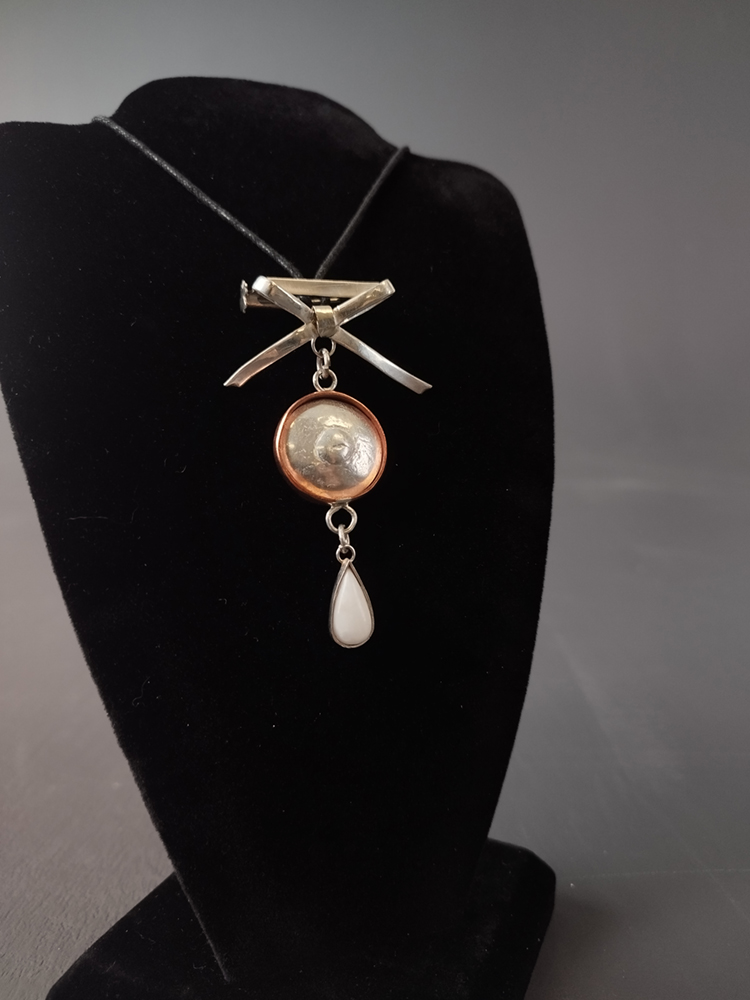 Necklace with a gold bow pendant, a disc pendant and a white teardrop stone pendant. Image courtesy of the artist