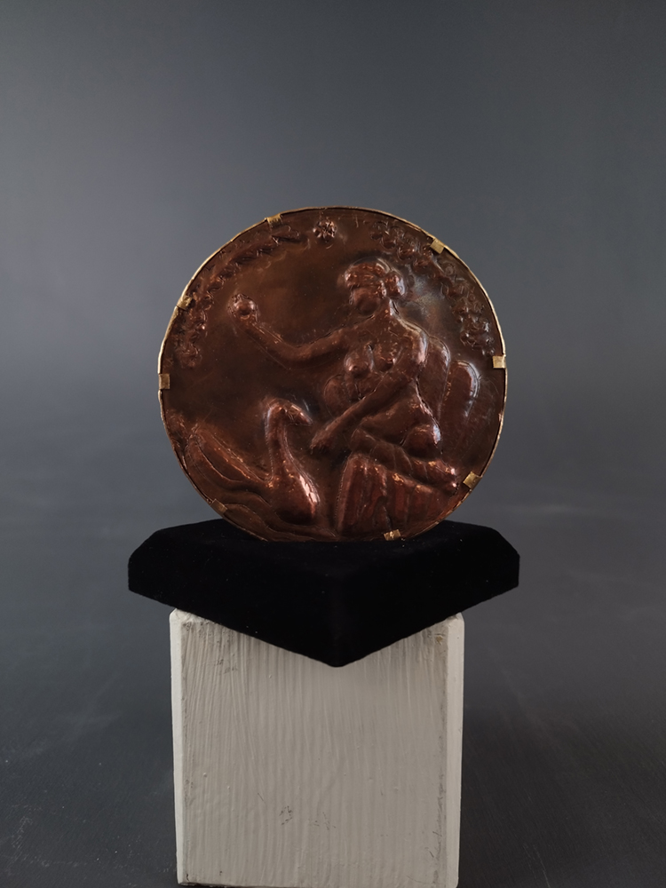 large copper disc featuring a woman in relief looking at herself in a mirror. Image courtesy of the artist