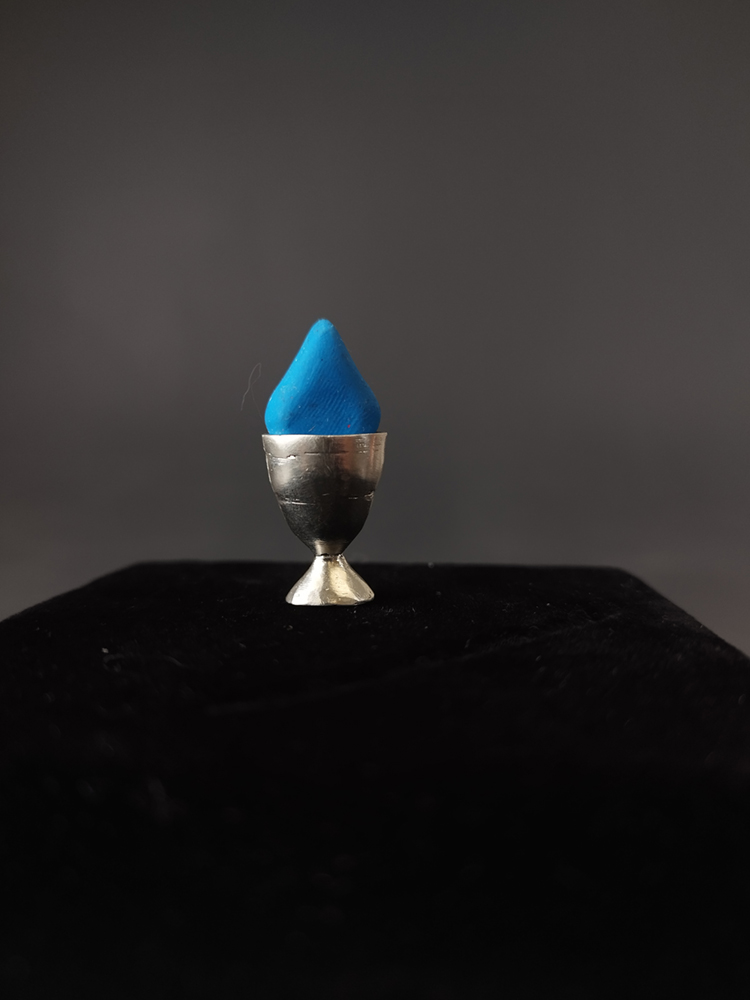 Depiction of a blue triangular pill in a metal cup. Image courtesy of the artist