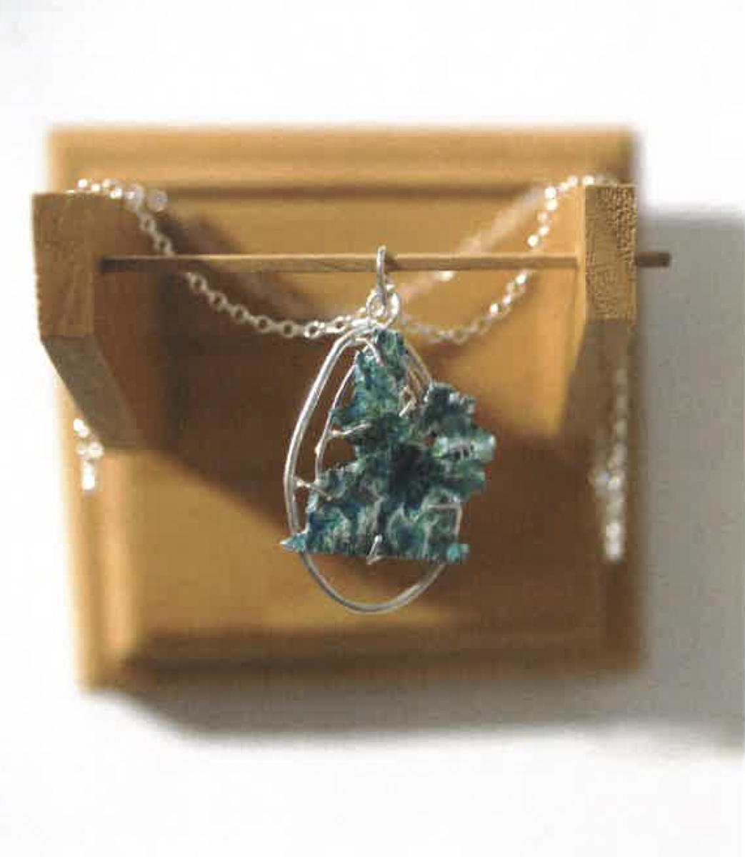 Delicate green enamel pendant resembling topography on a silver chain. Image courtesy of Naomi Hutchquist