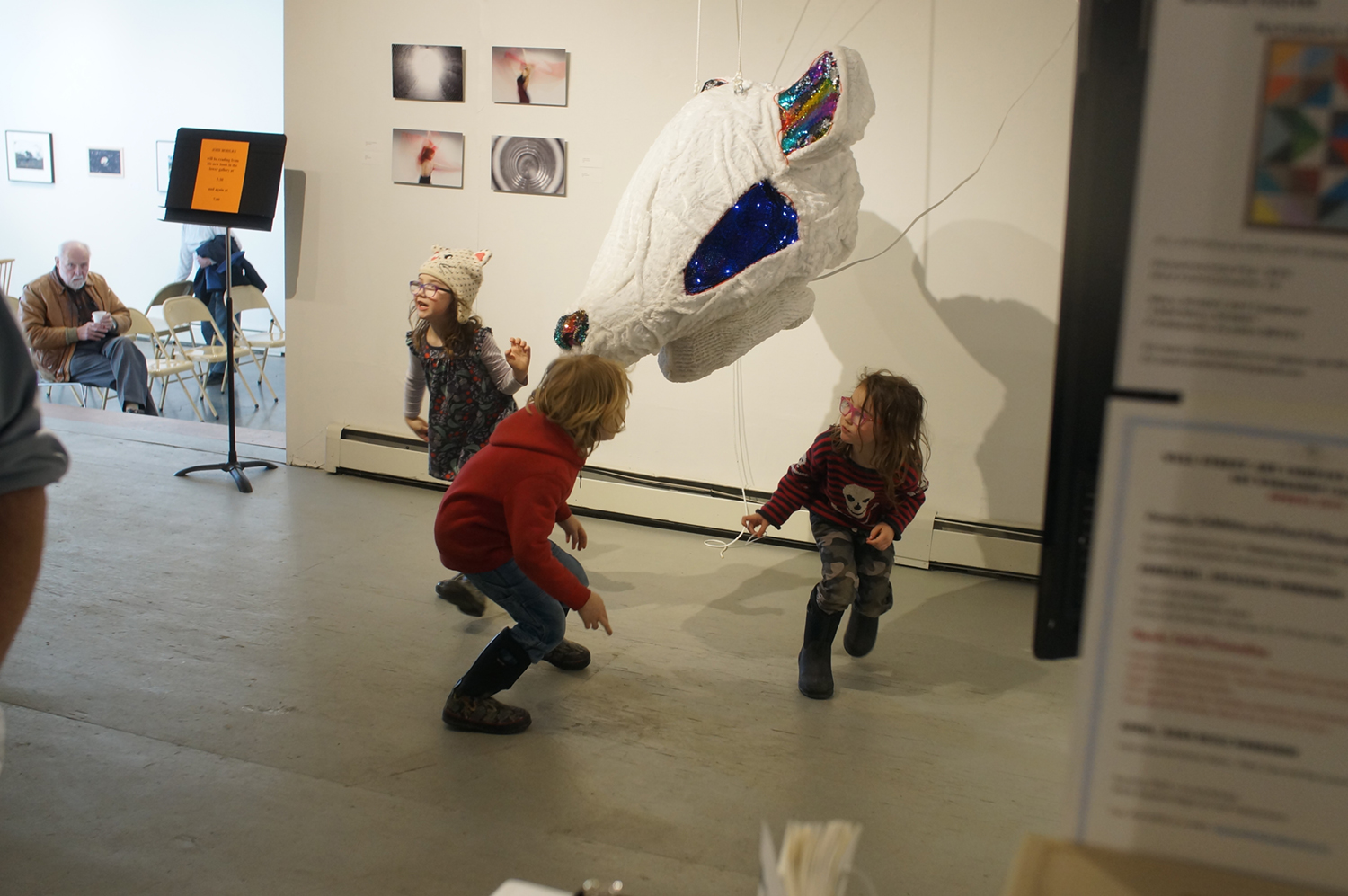 Kids play around the Who Are You? Who Am I? giant mouse head mask on display at Naomi Hutchquist's Naomi talks with attendees of her gallery opening of her BFA thesis exhibition Wheels of Life. Image courtesy of Naomi Hutchquist 
