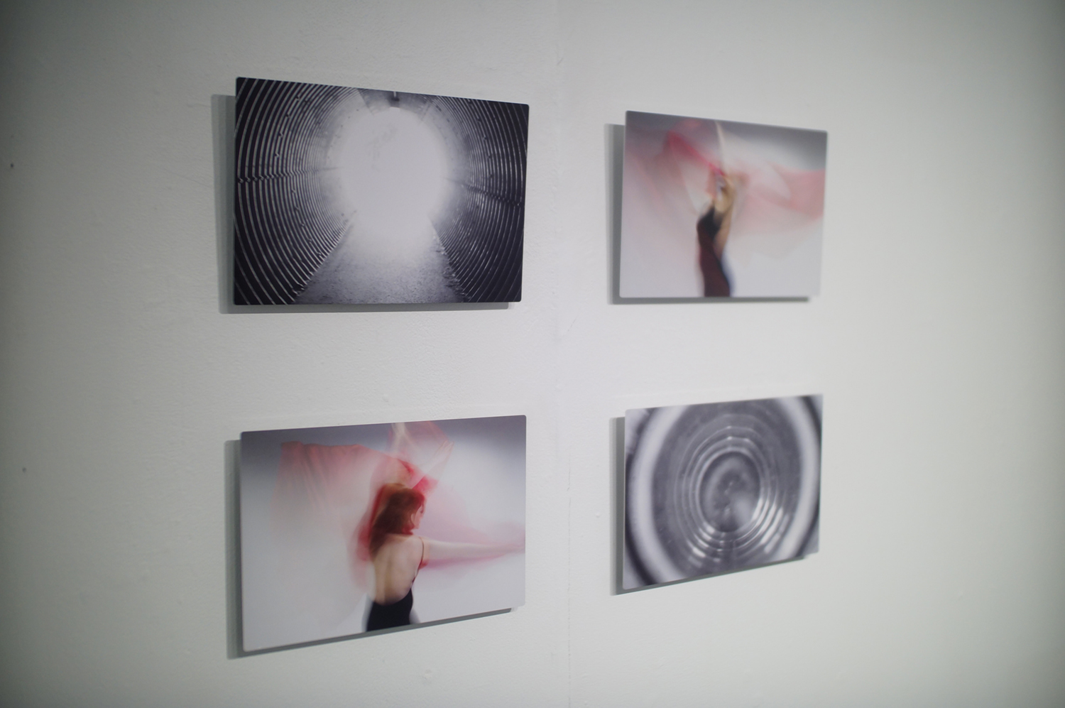 A grid of two-by-two photographs printed on aluminum hanging on a wall. Two look like black and white images of tunnels or portals. The other two are long exposure motion blurred portraits. Image courtesy of Naomi Hutchquist