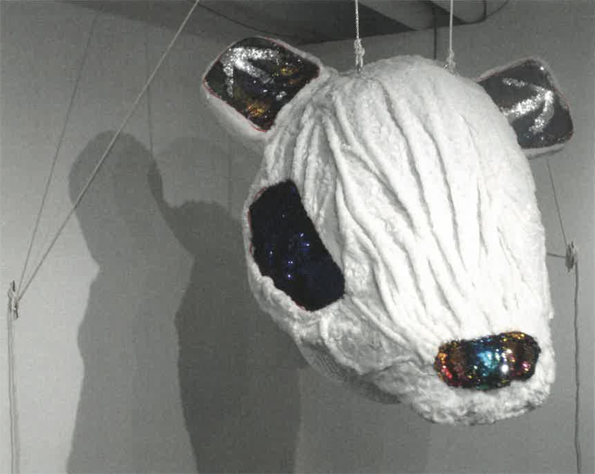 Large wearable sculpture of a white mouse head with sequin eyes, nose and ears, suspended from the gallery ceiling. Image courtesy of Naomi Hutchquist
