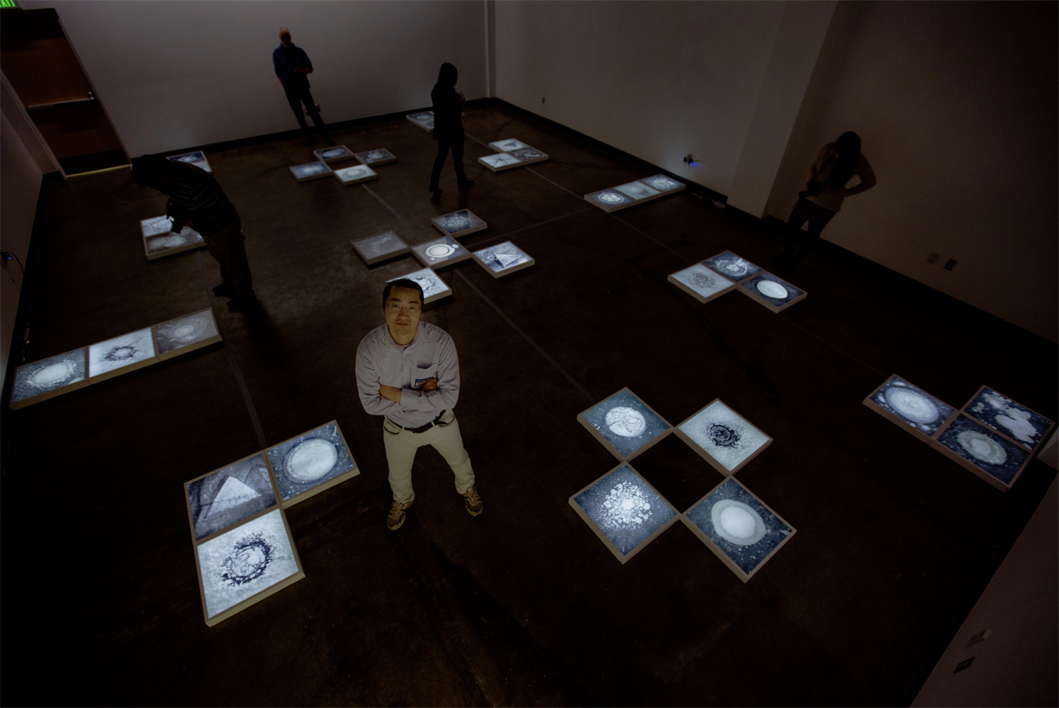 Ryota Kajita standing in the UAF Art Gallery amidst his installation of his MFA thesis show, Ice Formations. Images from Ice Formations were backlit and placed on the floor. Image courtesy of the artist