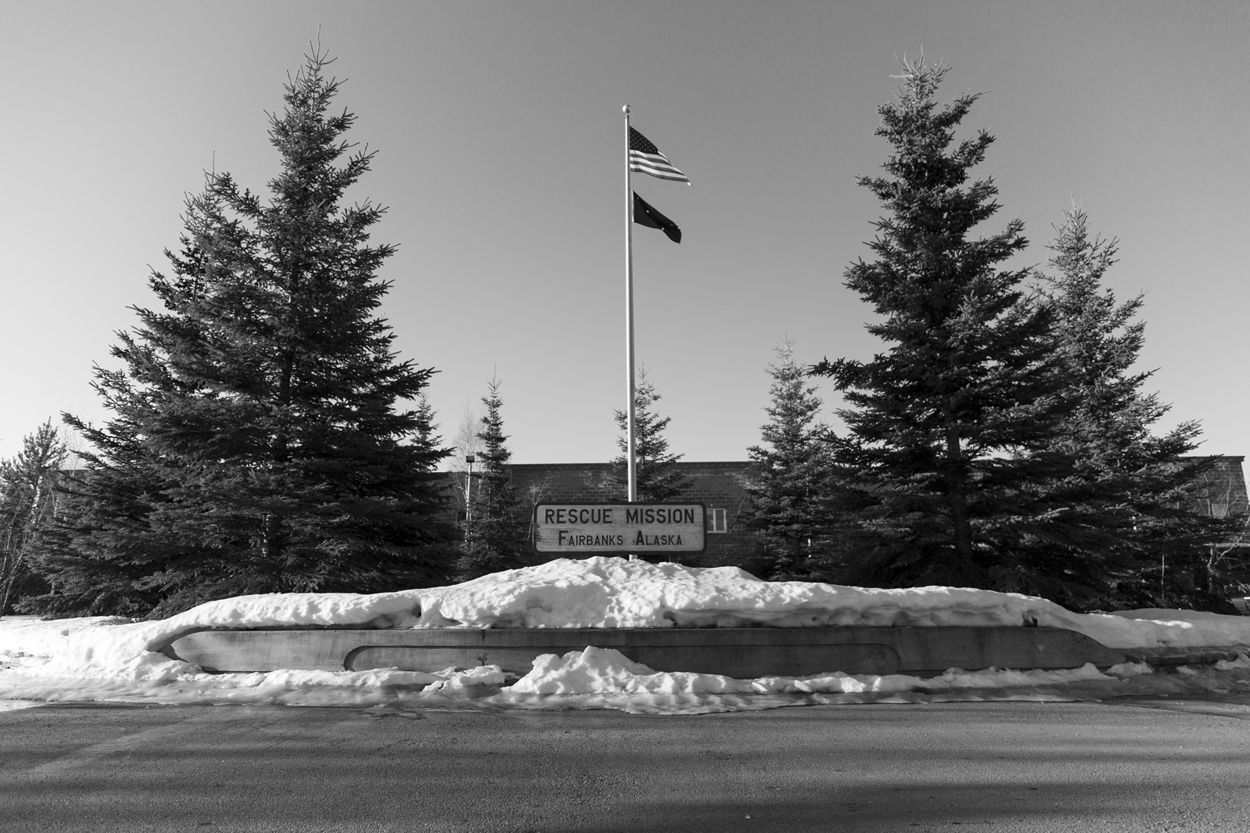 A strong wind blows both the Alaska state flag and American flag on April 18th, 2018 in Fairbanks, AK in front of the Rescue Mission. Courtesy of the artist