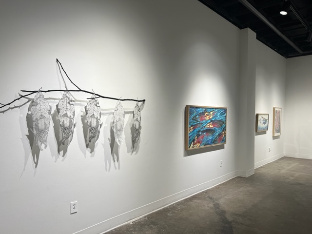 Framed paintings and paper cut outs of leaf/salmon hybrid images (Beauty of Decay: A Catalyst For Change)hang on the wall of the UAF Art Gallery during Susan Andrews' MFA exhibition, The Cascade Effect. Image courtesy of the artist