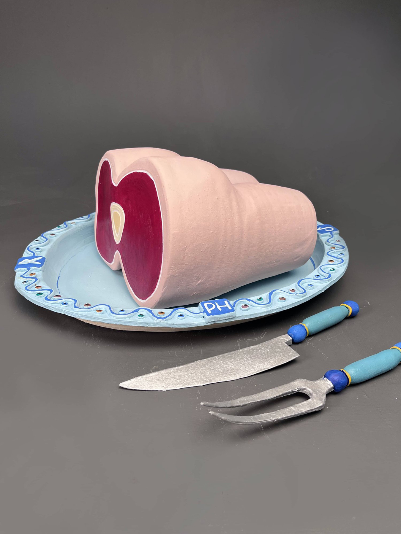 Ceramic sculpture of a cross-section of the female body on a blue platter next to a fork and knife, courtesy of the artist