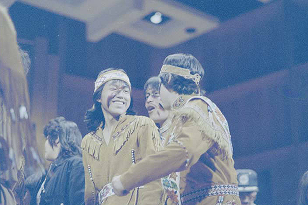 Several performers in traditional fringed moosehide jackets and headbands laugh during an early Festival of Native Arts. Alaska and Polar Regions Collections, Elmer E. Rasmuson Library, University of Alaska Fairbanks.