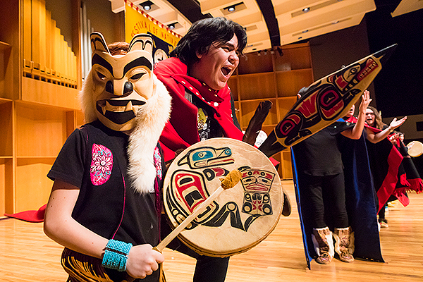 A young person performs in a traditional mask and with a drum alongside a dancer with a traditionally decorated paddle at the 2018 Festival of Native Arts. UAF photo by JR Ancheta.