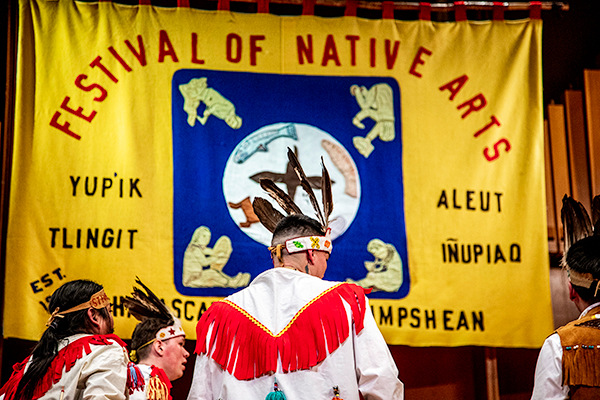 Participants in the 2023 Festival of Native Arts stand on stage under a banner naming the major Alaska Native groups. UAF photo by Marina Santos.