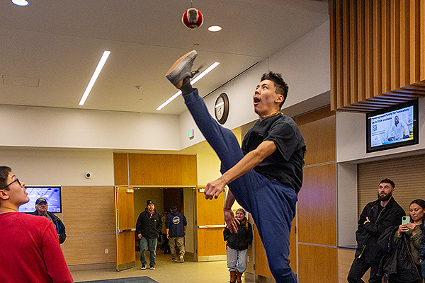 Spectators watch a performer demonstrate a high kick, aiming to touch a ball suspended from a pole, during day two of  the 2024 Festival of Native Arts. UAF photo by Eric Engman.