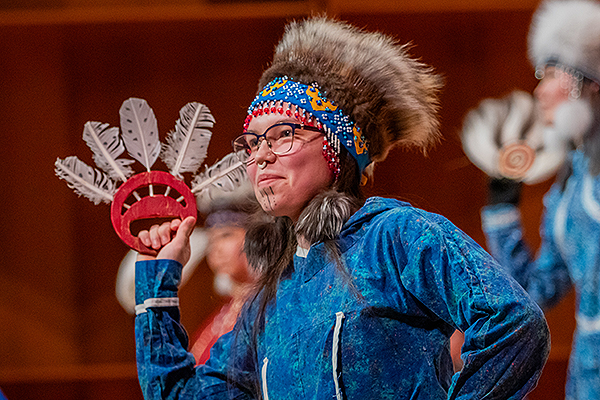 A woman in traditional attire, holding a feather-decorated hand fan and wearing intricate headgear and face paint, performs during day one of the 2024 Festival of Native Arts. UAF photo by Marina Santos.