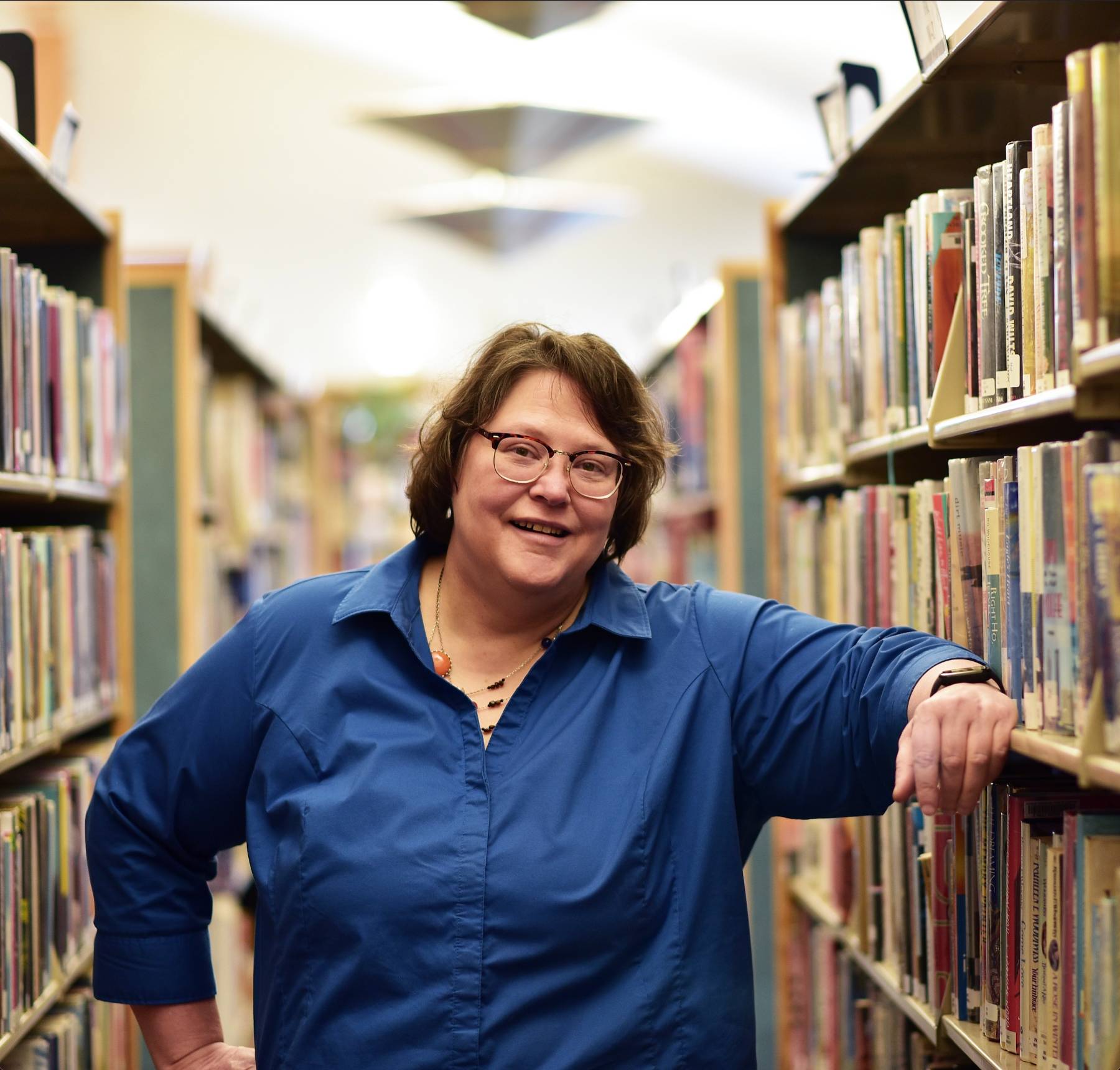 Carolyn Goolsby smiles in front of a shelf of books