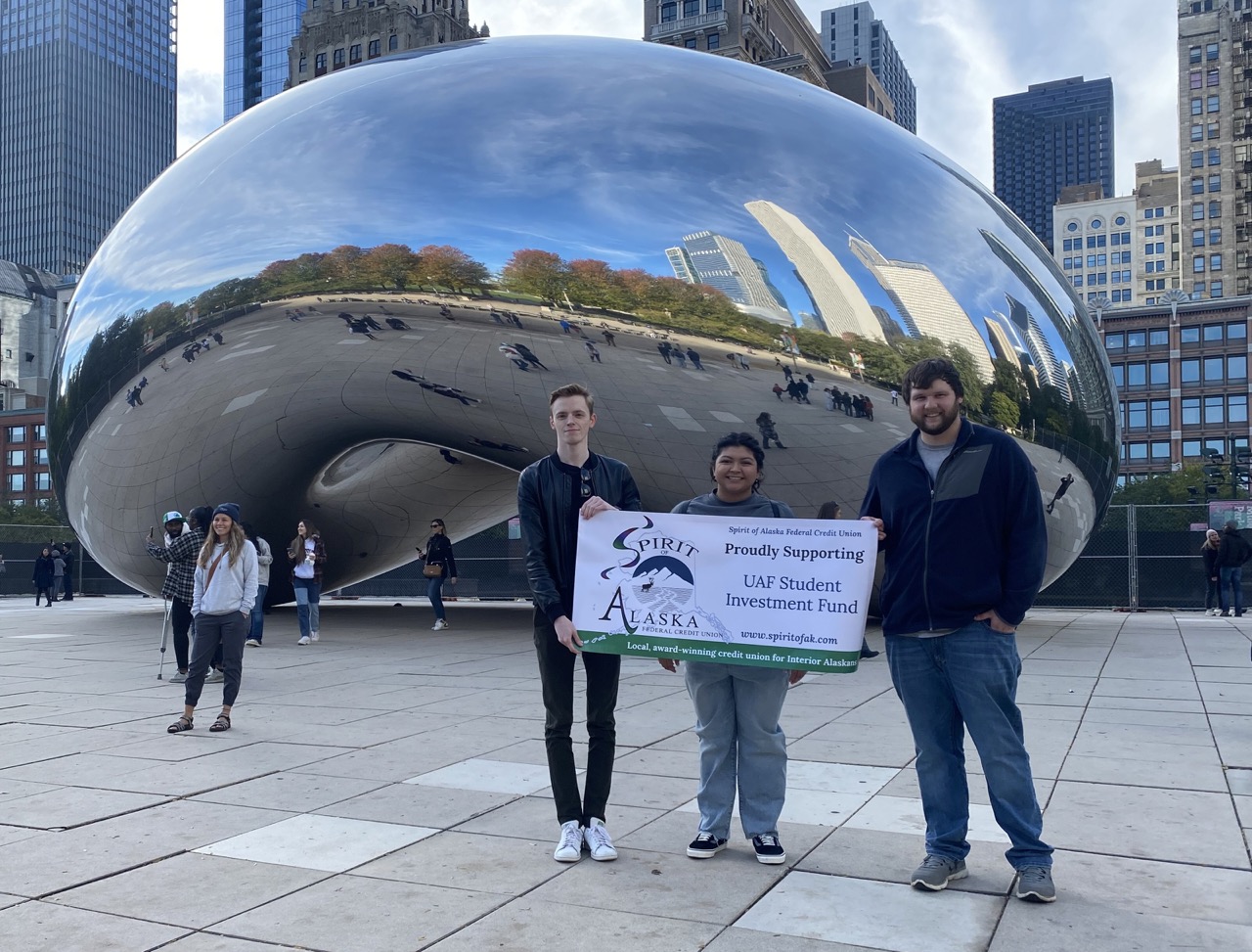 three students stand in front of famous silver sculpture in the city