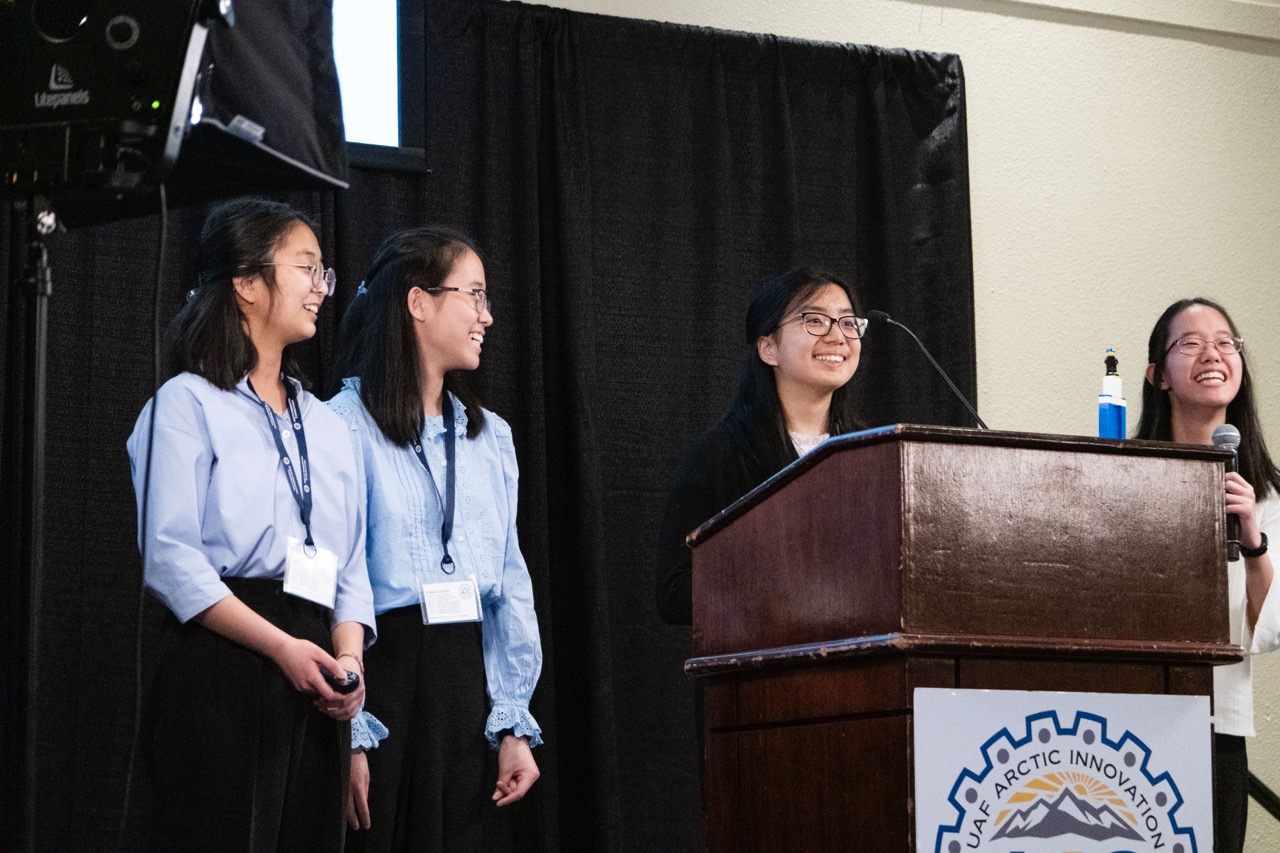 four smiling students present together on stage at a pitch competition