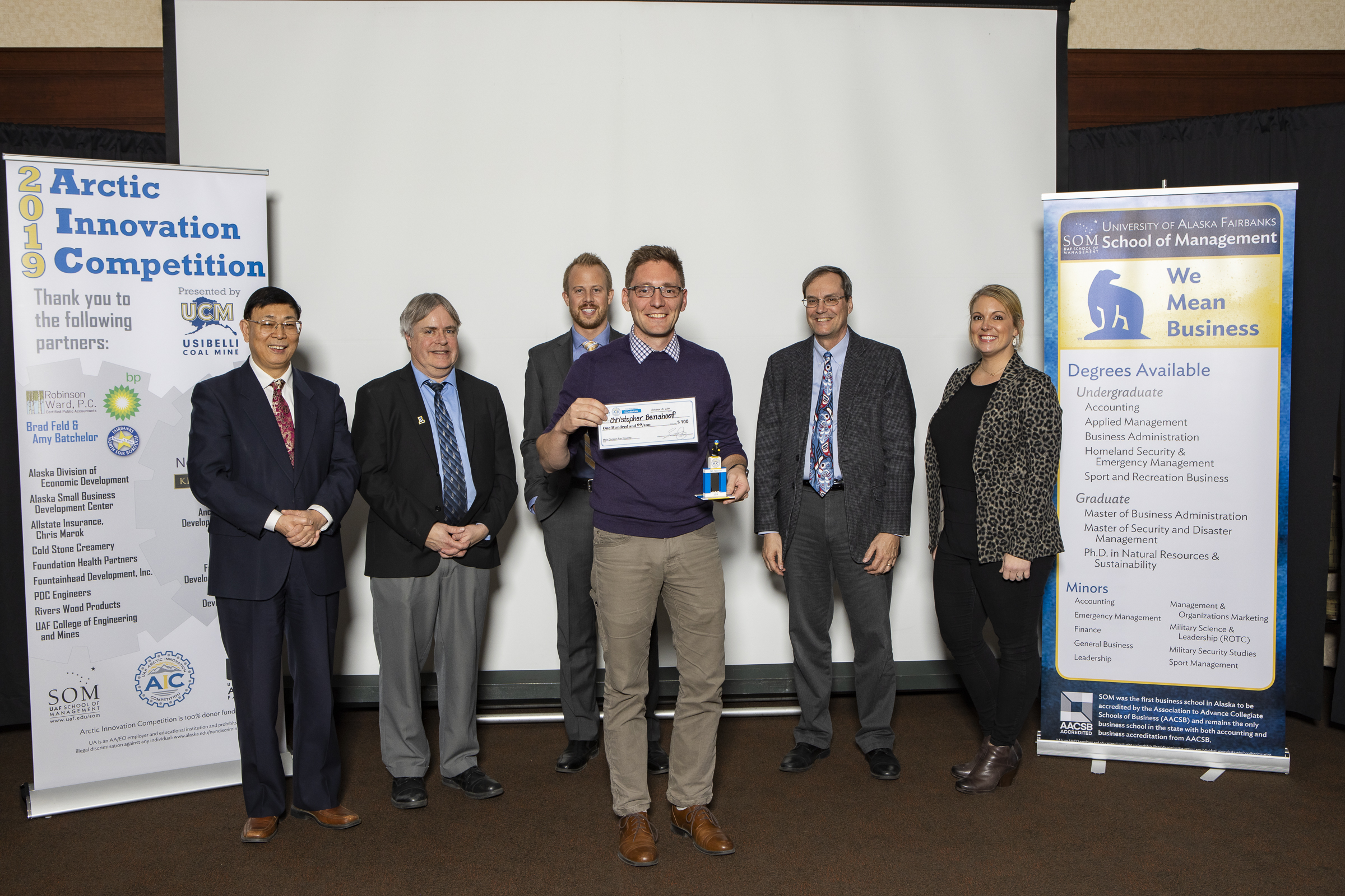 man stands with check and lego trophy in front of UAF professors and donors