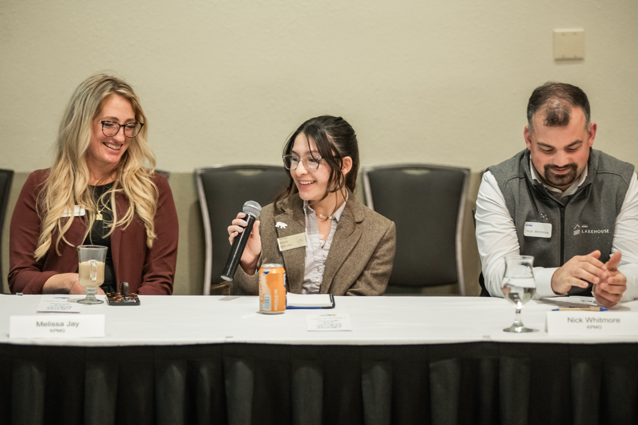 student holds mic to speak on a panel in between two professionals